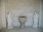 Une ancienne cuve baptismale en pierre entourée de deux statues d'anges.