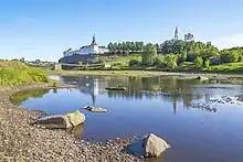 Deux collines sur lesquels reposent à gauche une église fortifiée et à droite un château. En arrière-plan se trouve une montagne enneigée.