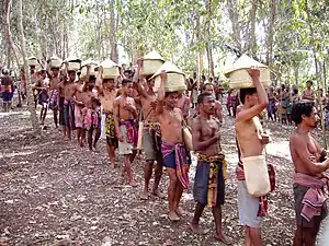 Sur le chemin du retour au village. Chaque personne représente un clan. Un clan est composé de plusieurs familles qui, ensemble, forment le village. La main gauche sur la poitrine signifie que la cérémonie est faite de bon cœur, avec honnêteté, confiance et des intentions pures. Tous les hommes ici portent les paniers à la manière des femmes. Dans la vie quotidienne, c'est la façon dont elles transportent leurs marchandises.