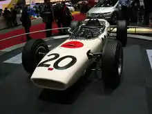 Photographie de la Honda RA271 blanche, avec un cercle rouge (du drapeau japonais), vue de trois-quarts, dans un musée d'exposition.