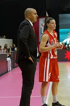 Homme en costume debout, les mains sur les hanches.