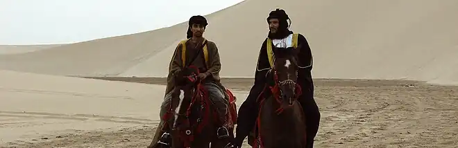 Photo panoramique de deux cavaliers dans le désert.