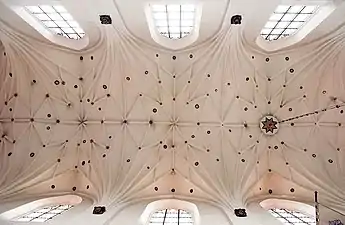 Photographie en contre-plongée d'une voûte blanche à nervures décorée d'étoiles.