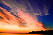 Le soleil couchant avec beaucoup de nuages rouges et une montagne.