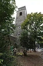 Clocher massif de base carrée dominant un parc boisé.
