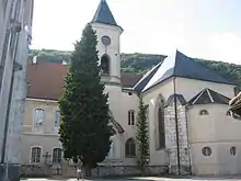 Photogaphie couleur du clocher et du chevet d'une église, dominant un petit cimetière planté d'arbres.