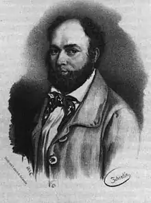 Noir et blanc, en chemise blanche avec nœuds papillon multicolore et un manteau beige. Visage bronzé rond avec barbe complète frisée, cheveux bruns avec calvitie, yeux foncés, nez aquilin.