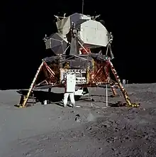 Photographie en couleur d'Aldrin en combinaison lunaire affairé près du module lunaire.