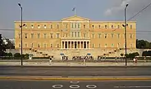 Photographie en couleurs montrant un bâtiment jaune à quatre étages bâti sur une sorte de terrasse.