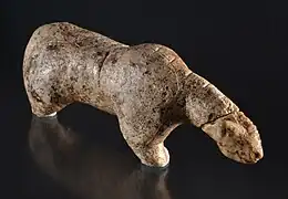 Photographie en couleurs sur fond noir et vue du dessus d'une statuette en ivoire représentant un ours des cavernes, ses pattes amputées reposant sur un socle de verre.