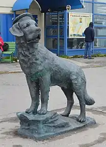 Statue représentant un saint-bernard debout les pattes avant posées sur quelques strates de roche.
