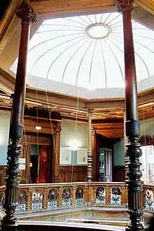 Espace octogonal avec portes et balustrades en bois. Verrière au plafond qui éclaire.