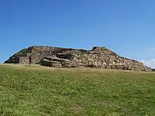 Vue de trois-quarts de l'ensemble du cairn, proue en premier plan. À la proue, la série de grosses dalles verticales du parement médian. Sur l'arrière du cairn, la partie détruite montre en coupe l'étagement des trois parements.