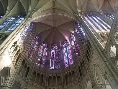 Vue en contre-plongée de la claire-voie de l'abside. En bas de l'image, le triforium consistant en une galerie en pierre avec de grandes ouvertures sur le chœur. Au-dessus, les verrières des 7 fenêtres de la claire-voie de l'abside. En haut de l'image, les voûtes de l'abside et du chœur.
