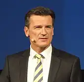 Photo de Bernhard Wolfgang en costume, vu de face devant un fond bleu.