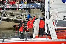 Dans le chenal des Sables-d'Olonne, debout, de face, à l'avant de son bateau, il salue la foule.