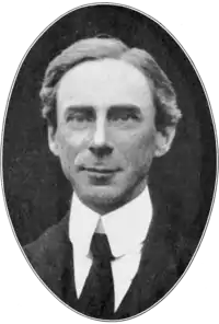 Portrait photographique en noir et blanc, dans un médaillon ovale, d'un homme souriant, portant un haut col rigide et une cravate noire.