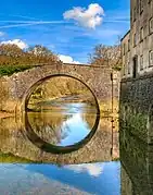 Photo d'un pont de briques jaunes à une arche enjambant une rivière. L'arche et son reflet forment un cercle parfait