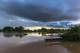Nuages bleus orageux au-dessus du Mékong au coucher du soleil avec réflexion dans l'eau et une pirogue amarrée à la berge, à Don Det. Juillet 2020.