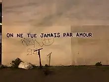 Un collage de la phrase "On ne tue jamais par amour" sur un mur avec une lumière de coucher de soleil.