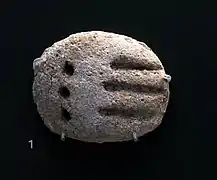Petite tablette arrondie comprenant des signes ronds et linéaires.