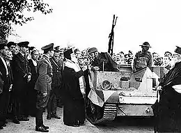 Un dignitaire orthodoxe bénissant les occupants d'une chenillette, sous les yeux de nombreux hommes, dont des soldats.