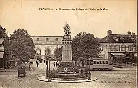 Carte postale ancienne montrant une motrice du Tramway de Troyes derrière le Monument des Enfants de l'Aube, et, en arrière plan, la Gare
