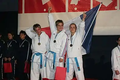 L'équipe de France de kata féminin victorieuse aux championnats du monde de karaté seniors 2006. À gauche : Jessica Buil. Au milieu : Sabrina Buil. Sabrina Buil, au centre, brandit le poing d'un air victorieux.