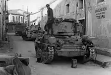 Deux blindés dans une rue, avec un officier allemand debout sur le premier de ceux-ci.