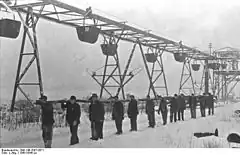 Photographie ancienne en noir et blanc montrant une file d'hommes portant un tuyau.