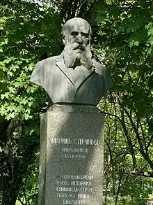 Buste d'un homme barbu dans un parc public.