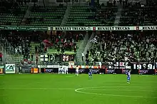 Photo montrant des personnes dans une tribune, derrière des joueurs de football en premier plan