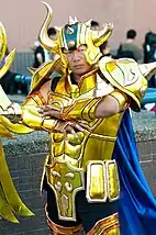 Homme à l'air sévère portant une armure dorée sophistiquée, avec un casque à corne, lui aussi doré.