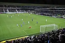 Vue générale du terrain depuis le derrière d'un but, l'action se déroulant sur le but du premier plan.