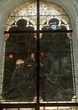 Photographie en couleurs d'un vitrail représentant un corps transporté par des hommes.