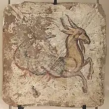 Photo en couleur d'une peinture sur brique représentant une créature avec partie arrière du corps de poisson et partie avant de tête et pattes de chèvre. La créature est peinte en jaune avec contours noirs et des traits rouges orangés donnent du relief