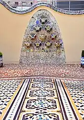 Mosaïques sur le sol et le fond d'une jardinière. Profil de mur en volutes.