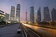 Gratte ciel illuminés de nuit. Au milieu, une autoroute contrebalance la verticalité des bâtiments.