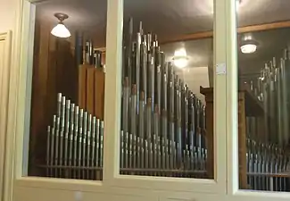 Photographie en couleurs de rangées de tuyaux d'orgues derrière une cloison vitrée