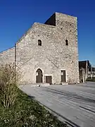 Photographie en couleurs d'un petit édifice en moellons flanqué d'une tour massive.