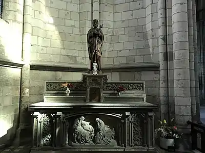 Autel présentant, en bas de l'image, un bas-relief représentant un homme et une femme pleurant autour d'un corps. Sur l'autel, deux statues d'hommes barbues et quelques pots de fleurs.