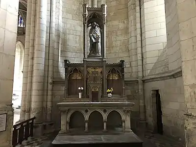 Autel présentant des petites murailles sculptées et surmontée d'une femme vêtue de bleu et apprenant à une petite fille à lire.