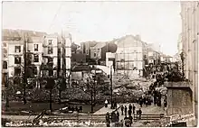 Photo noir et blanc de bâtiments en ruine avec des personnes passant à proximité
