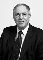 Portrait en noir et blanc d'un homme en costume portant des lunettes.