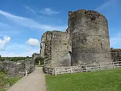 Photo d'un bâtiment en ruines aux murs en pierre grise, avec une grande tour ronde sur la droite