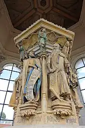 Photo de statues colorées placées autour d'un pilier central.