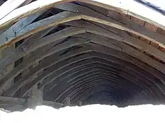 Photographie en couleurs de la charpente d'un long bâtiment.