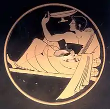 Fresque de couleur ocre et noire, abîmée en son centre et représentant un jeune homme assit sur une chaise longue, vêtu d'une toge et tenant un vase dans sa main.