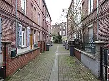 Photographie en couleur représentant deux rangées face à face de petites maisons mitoyennes de trois niveaux avec une poubelle individuelle devant chacune