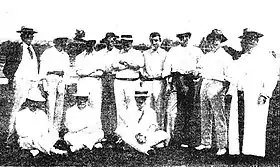 Photo d'un groupe d'hommes habillés en blanc. Neuf hommes sont debout et les trois autres sont assis devant eux.